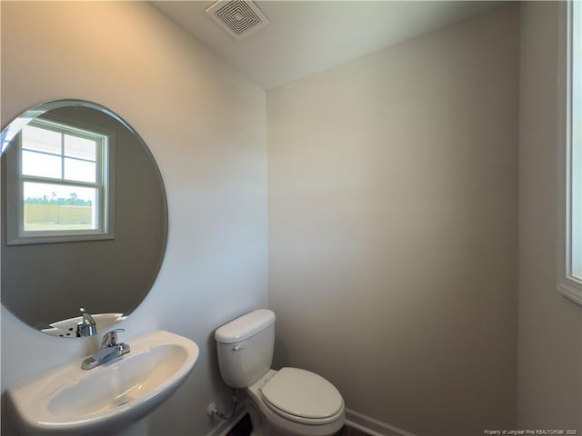 half bath with toilet, a sink, and visible vents