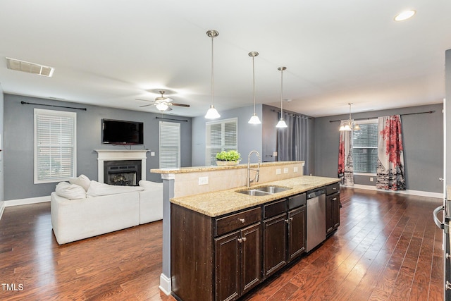 kitchen featuring dark hardwood / wood-style flooring, stainless steel dishwasher, sink, pendant lighting, and an island with sink