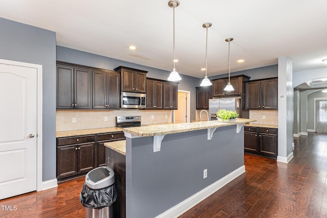 kitchen featuring stainless steel appliances, a kitchen breakfast bar, dark hardwood / wood-style flooring, an island with sink, and decorative light fixtures