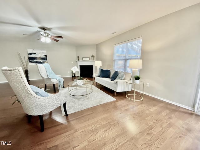 living room with ceiling fan, a fireplace, baseboards, and wood finished floors