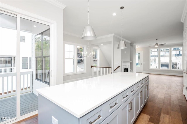 kitchen featuring a center island, ceiling fan with notable chandelier, ornamental molding, decorative light fixtures, and dark hardwood / wood-style flooring