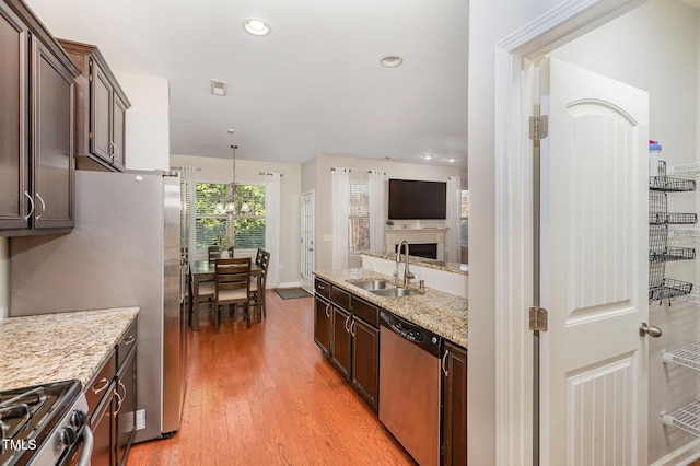 kitchen featuring sink, decorative light fixtures, light wood-type flooring, dark brown cabinets, and stainless steel appliances