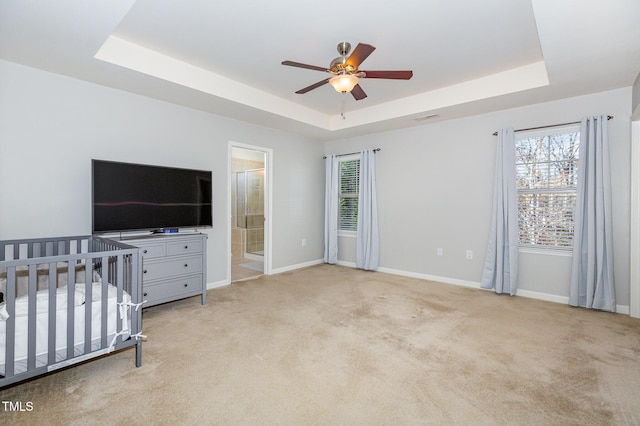 bedroom featuring a nursery area, ensuite bathroom, a raised ceiling, ceiling fan, and multiple windows