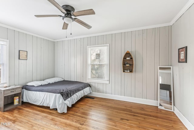 bedroom featuring wooden walls, hardwood / wood-style flooring, ceiling fan, and ornamental molding