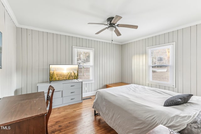 bedroom with ceiling fan, wood walls, light wood-type flooring, and ornamental molding