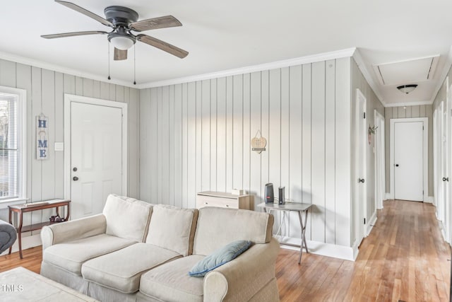 living room featuring crown molding, wooden walls, ceiling fan, and light hardwood / wood-style floors