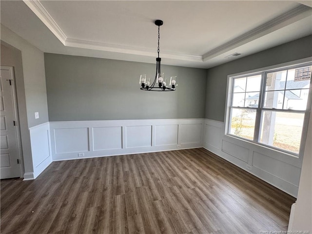 unfurnished dining area featuring a notable chandelier, a wainscoted wall, dark wood-style floors, a tray ceiling, and crown molding