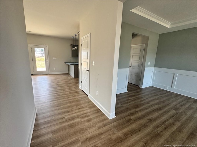 hallway featuring dark wood finished floors, a raised ceiling, a wainscoted wall, crown molding, and a decorative wall