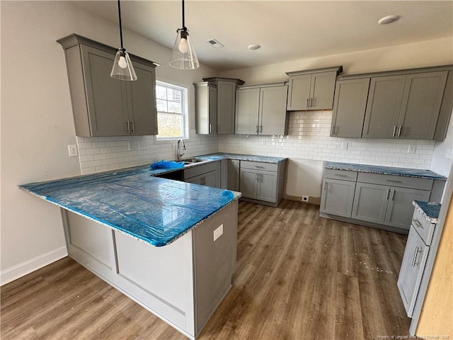 kitchen featuring decorative backsplash, dark wood-style flooring, a peninsula, gray cabinetry, and pendant lighting