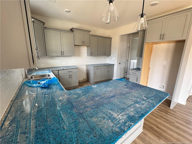 kitchen featuring decorative light fixtures, gray cabinets, light wood-style flooring, backsplash, and a sink