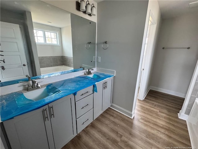 bathroom featuring a washtub, a sink, baseboards, and wood finished floors