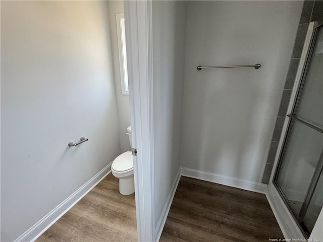 bathroom with a shower with shower door, baseboards, toilet, and wood finished floors