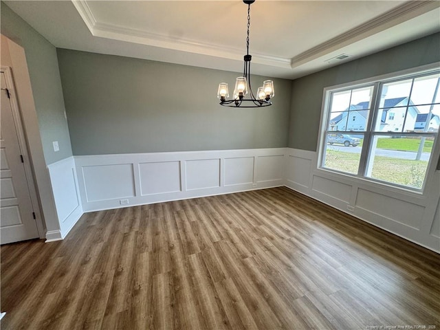 unfurnished dining area with an inviting chandelier, ornamental molding, visible vents, a raised ceiling, and wood finished floors