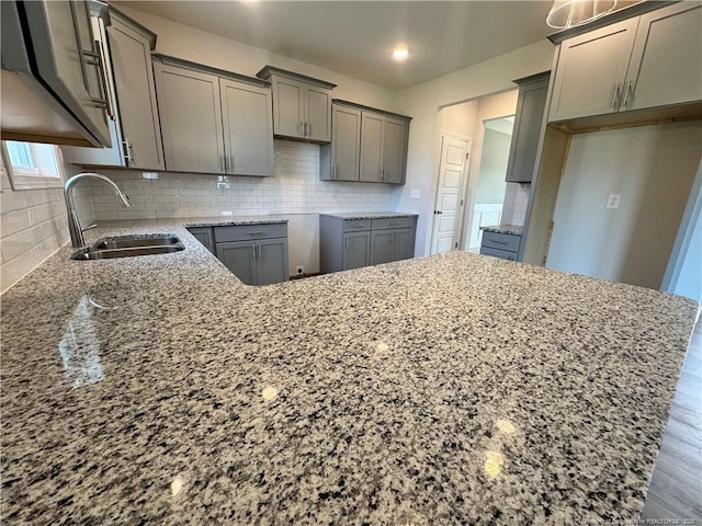 kitchen with light stone counters, gray cabinets, backsplash, a sink, and wood finished floors