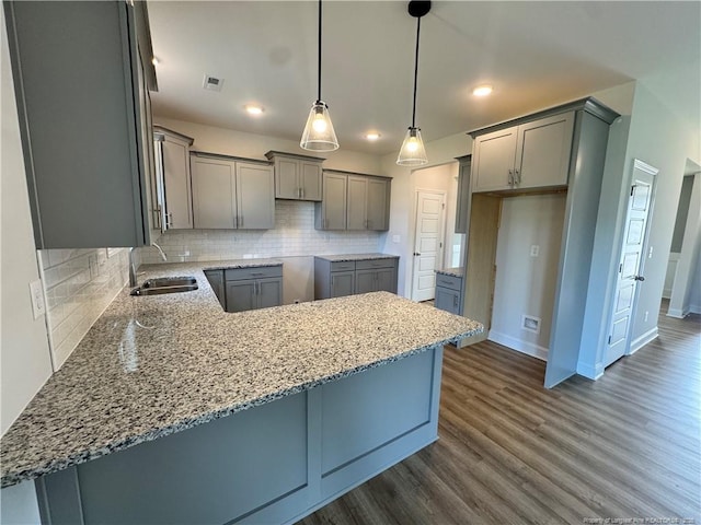 kitchen with light stone counters, dark wood-style flooring, a sink, gray cabinetry, and backsplash