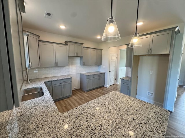 kitchen with a sink, gray cabinetry, wood finished floors, light stone countertops, and decorative backsplash