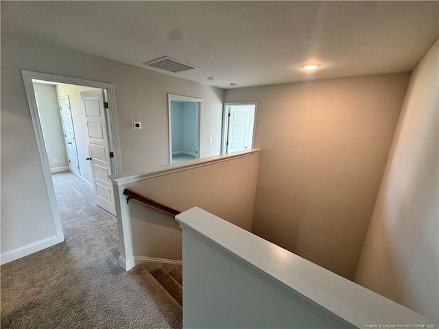 hallway featuring carpet flooring, an upstairs landing, visible vents, and baseboards