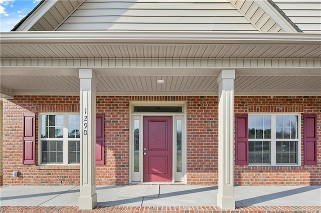 doorway to property with a porch and brick siding