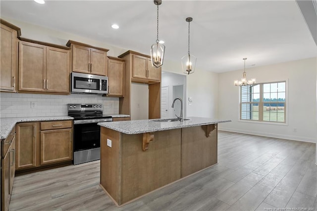 kitchen featuring a sink, light wood-style floors, appliances with stainless steel finishes, light stone countertops, and tasteful backsplash