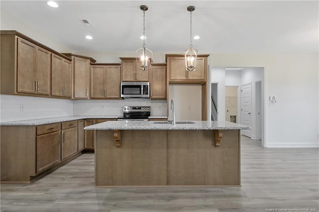 kitchen featuring a sink, visible vents, appliances with stainless steel finishes, decorative backsplash, and an island with sink