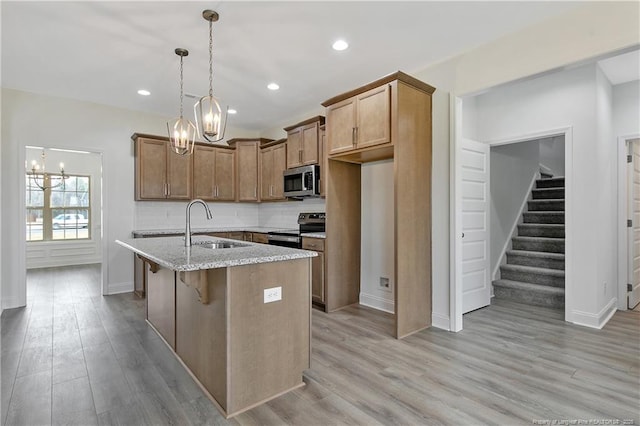 kitchen with a sink, light stone countertops, stainless steel appliances, light wood-type flooring, and backsplash