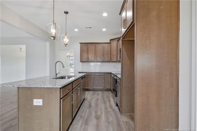 kitchen with light stone counters, a sink, appliances with stainless steel finishes, decorative backsplash, and a center island with sink