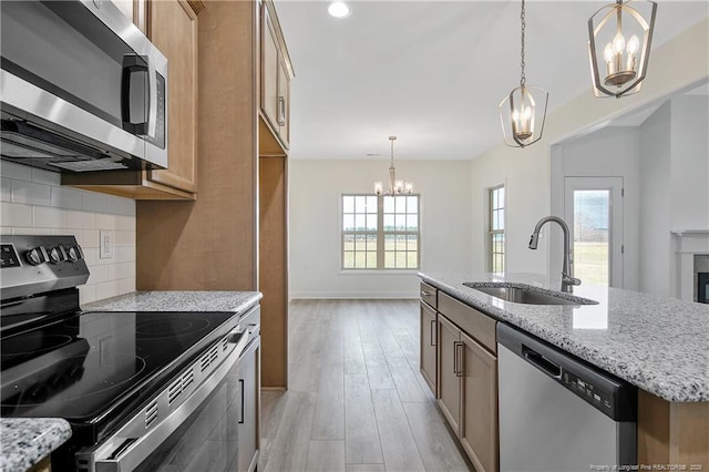 kitchen featuring tasteful backsplash, light wood-style flooring, light stone countertops, stainless steel appliances, and a sink