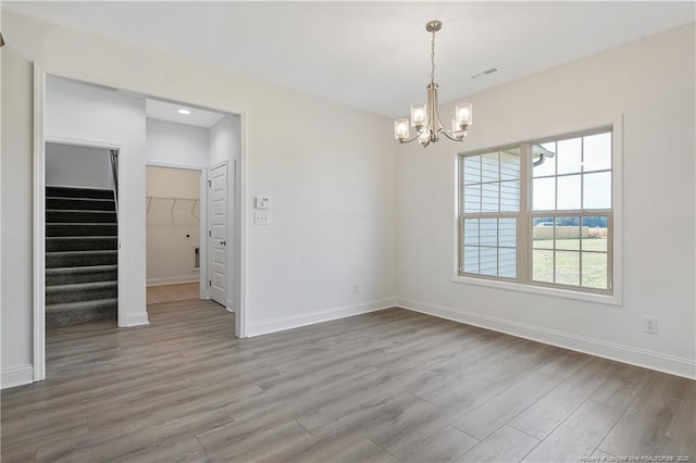 unfurnished dining area with stairs, an inviting chandelier, wood finished floors, and baseboards