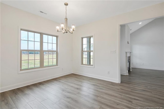 spare room featuring visible vents, baseboards, a glass covered fireplace, dark wood-type flooring, and an inviting chandelier