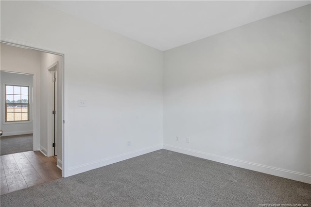 spare room with dark wood-style floors, dark colored carpet, and baseboards