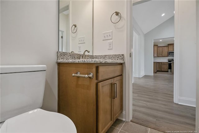 half bath featuring lofted ceiling, toilet, wood finished floors, vanity, and baseboards