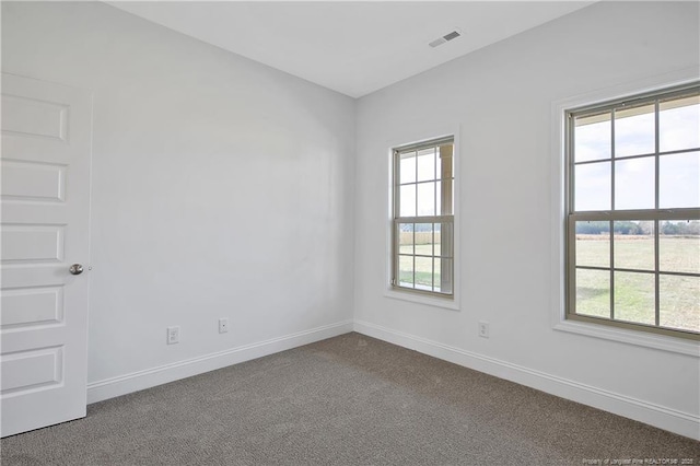 carpeted spare room featuring a wealth of natural light, visible vents, and baseboards