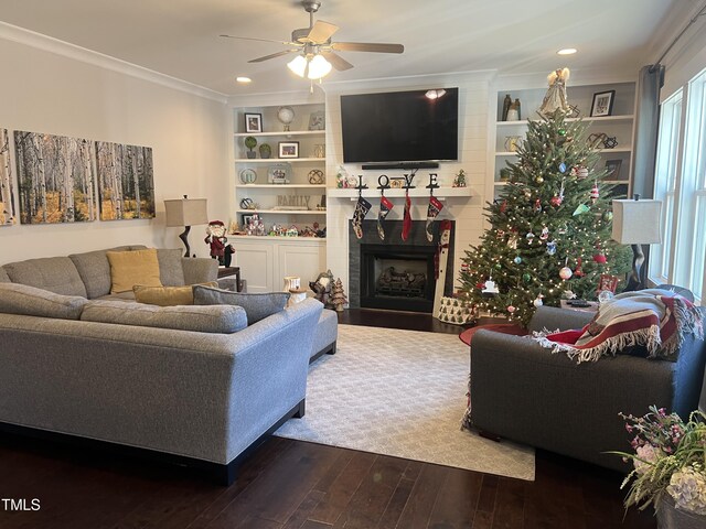 living room with built in shelves, dark hardwood / wood-style floors, ceiling fan, and crown molding