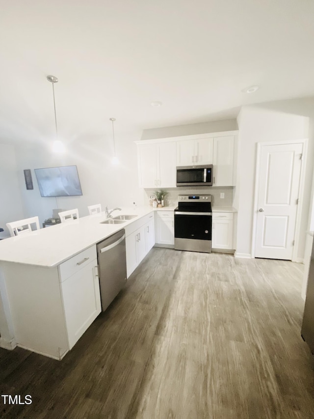 kitchen with white cabinetry, sink, stainless steel appliances, pendant lighting, and hardwood / wood-style flooring