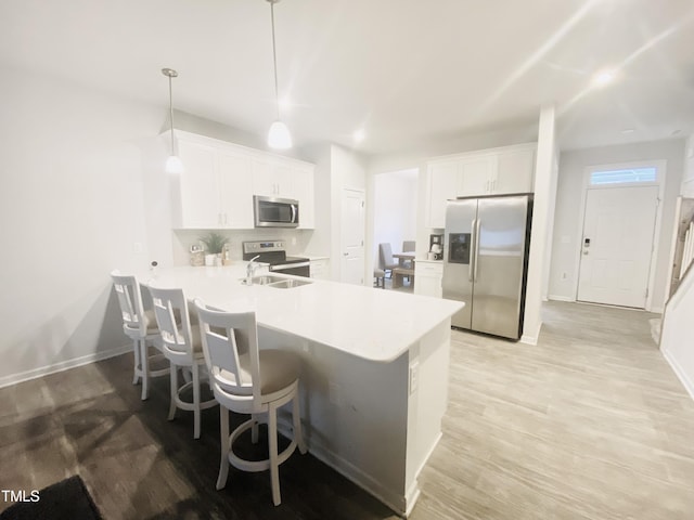 kitchen featuring white cabinets, hanging light fixtures, light hardwood / wood-style flooring, appliances with stainless steel finishes, and kitchen peninsula