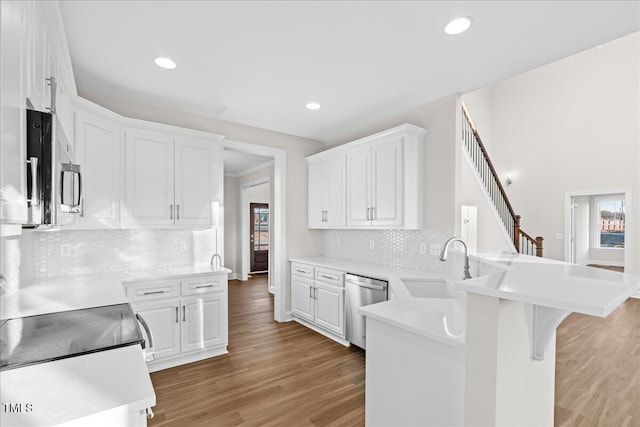 kitchen featuring white cabinets, hardwood / wood-style flooring, appliances with stainless steel finishes, kitchen peninsula, and a breakfast bar area