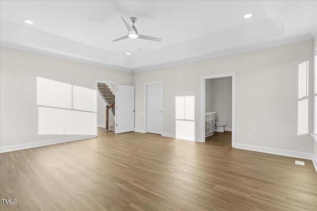 unfurnished living room featuring a raised ceiling, ceiling fan, and hardwood / wood-style floors