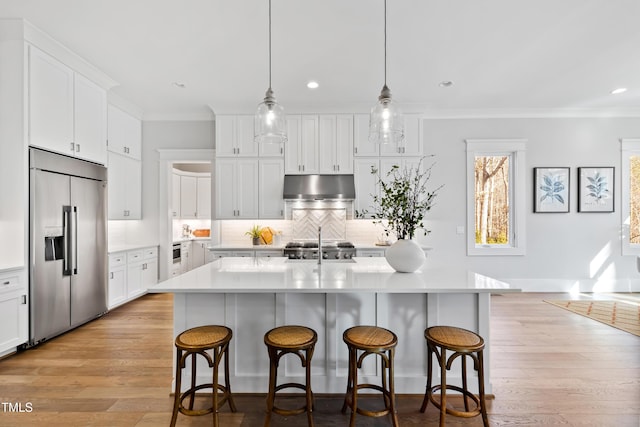 kitchen with built in refrigerator, white cabinetry, a center island with sink, and decorative light fixtures