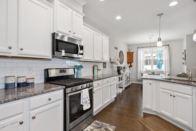 kitchen with white cabinetry, hanging light fixtures, stainless steel appliances, dark hardwood / wood-style flooring, and dark stone counters