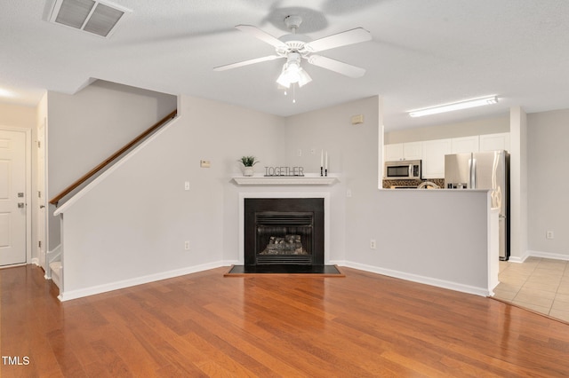 unfurnished living room with ceiling fan, light wood-type flooring, and a textured ceiling