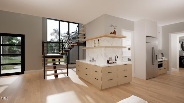 kitchen featuring wall oven, high end refrigerator, stacked washer / dryer, light hardwood / wood-style floors, and decorative backsplash