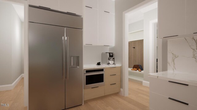 kitchen with light stone countertops, wall oven, stainless steel built in refrigerator, light hardwood / wood-style flooring, and white cabinetry