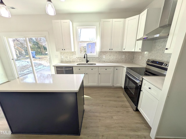 kitchen with wall chimney range hood, a wealth of natural light, sink, stainless steel appliances, and white cabinets