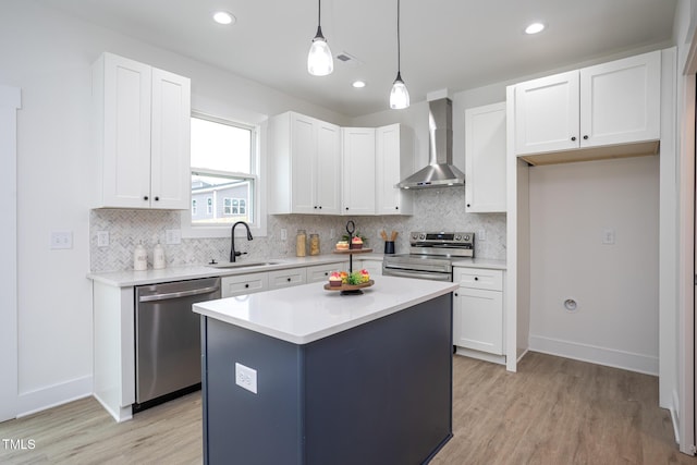 kitchen featuring a kitchen island, decorative light fixtures, white cabinetry, stainless steel appliances, and wall chimney range hood