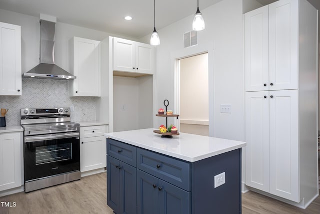 kitchen with stainless steel electric stove, white cabinetry, hanging light fixtures, light hardwood / wood-style floors, and wall chimney exhaust hood