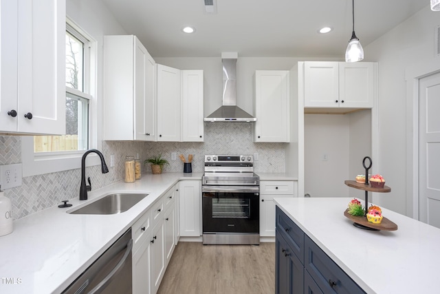 kitchen with sink, wall chimney range hood, pendant lighting, stainless steel appliances, and white cabinets