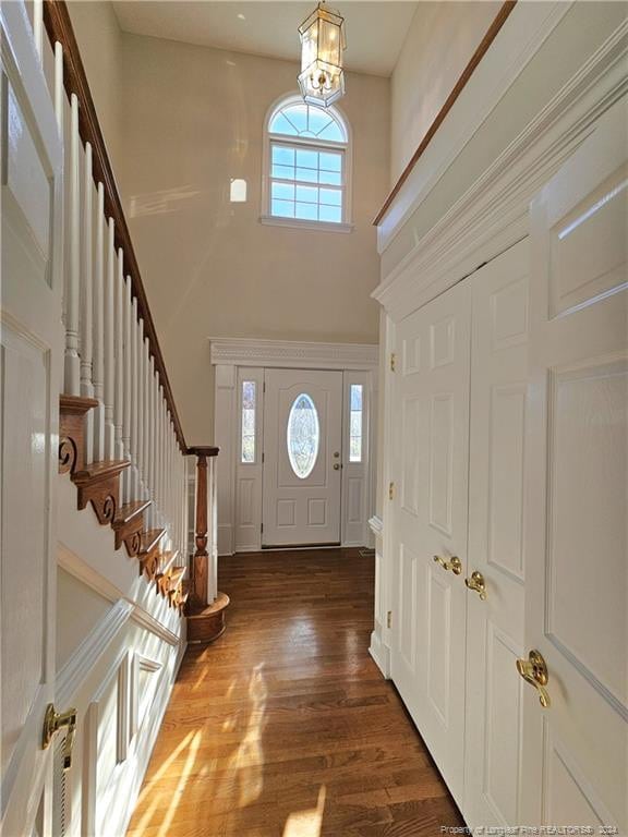 foyer featuring a wealth of natural light, a towering ceiling, a chandelier, and dark hardwood / wood-style floors