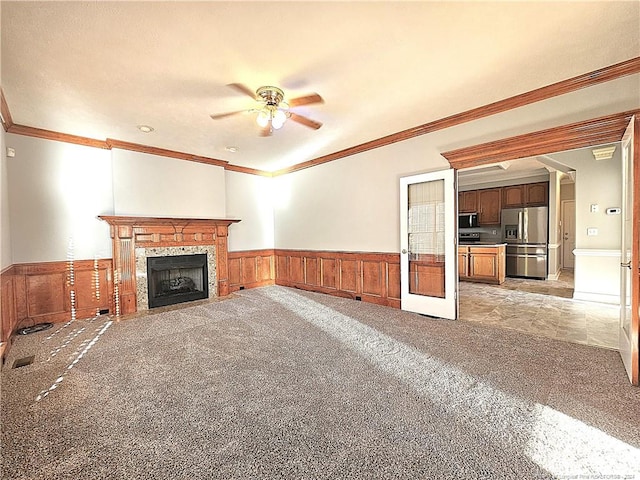 unfurnished living room with ceiling fan, ornamental molding, and light carpet