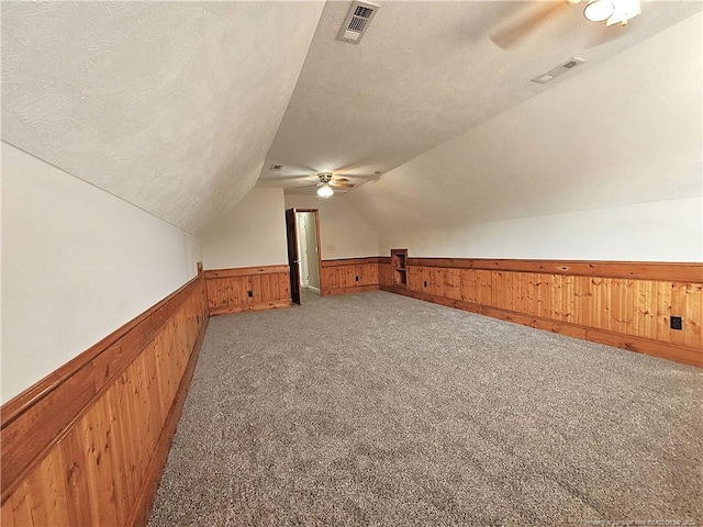 additional living space featuring a textured ceiling, wood walls, lofted ceiling, and light carpet