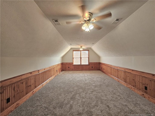 additional living space with carpet flooring, a textured ceiling, ceiling fan, lofted ceiling, and wood walls